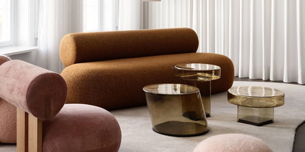 Ein langes, abgerundetes Sofa steht vor gl&auml;sernen Beistelltischen